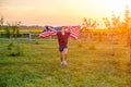 Carefree child running in field with blowing American flag in hands at sunset Royalty Free Stock Photo