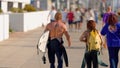 A carefree couple strolls along the vibrant venice beach sidewalk, surfboards in hand, their clothing a mix of laid-back