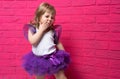Carefree cute little girl in tutu skirt giggling covering her mouth with her hand on pink background Royalty Free Stock Photo
