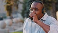 Carefree emotional senior African American man sitting outdoor relishing weekend in park drinking coffee having fun