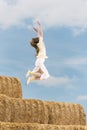 Carefree girl jumps from high haystack. Happy young woman has fun on the farm. Blue sky background Royalty Free Stock Photo