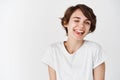 Carefree girl with short hair, winking and showing tongue with silly happy face, standing happy in t-shirt against white