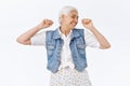 Carefree, happy, lively joyful senior woman with grey hai, raising hands up, fist pump or stretching feeling cheerful