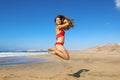 Carefree healthy bikini woman jumping on the beach. Happy smiling girl doing a jump of freedom and happiness in a free body on