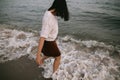 Carefree hipster woman walking barefoot in sea waves on beach. Feet in water foam. Mindfulness