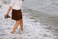 Carefree hipster woman walking barefoot in sea waves on beach, with flip flops in hand. Mindfulness Royalty Free Stock Photo