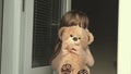 Carefree kid hugs his toy. A child in the spring plays with a toy at an open window on windowsill. Little girl in summer