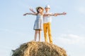 Carefree little girl and boy standing at top of haystack spreading arms wide. Friends dream to fly. Freedom. Blue sky. Royalty Free Stock Photo