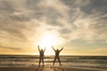 Carefree multiracial senior couple jumping with arms raised at beach against sky during sunset