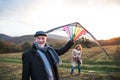 Carefree senior couple flying a kite in an autumn nature at sunset.