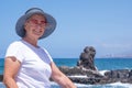 Carefree senior woman sitting at the beach enjoying summer vacation, wearing blue cap and pink sunglasses. Relaxed retiree looking