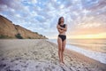 Carefree smiling brunette woman in black swimwear standing on beach, sunny summer day Royalty Free Stock Photo