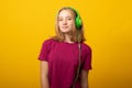 Carefree smiling young girl listens music in headphones isolated over vivid yellow background