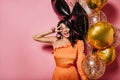 Carefree tanned girl enjoying party with smile. Charming latin woman with balloons laughing on pink background