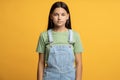 Intelligent schoolgirl with unemotional glance isolated on orange background looking at camera Royalty Free Stock Photo