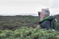 A carefree white-haired senior man in excursion at the mountain looking at the horizon over sea. Active retiree backpacker