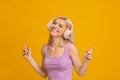 Carefree woman in headphones dacing to her favorite music and smiling on yellow studio background