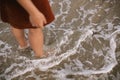 Carefree woman standing barefoot in sea waves on beach. Feet in water with foam, summer vacation Royalty Free Stock Photo