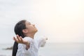 Carefree young Asian girl taking deep breath for natural blissful fresh air facing against sky, opening arms relaxing on the sea