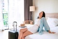 Carefree young Asian traveler woman relax on bed in hotel room. Travel alone, summer and vacation concept Royalty Free Stock Photo