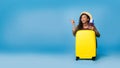 Carefree young black woman holding passport and tickets, sitting behind suitcase, ready to travel on blue background Royalty Free Stock Photo