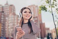 Carefree young lady is listening to favourite song on her smartphone outdoors, walking on the spring street, wearing cozy outfit,