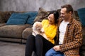 carefree young couple in casual clothing bonding with domestic cat and smiling while resting on the sofa indoors Royalty Free Stock Photo