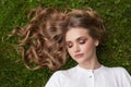 Carefree young woman with curly blonde hair lying on green grass outdoor Royalty Free Stock Photo