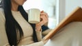 Carefree young woman in warm sweater drinking hot tea and reading book Royalty Free Stock Photo