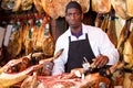 Careful seller cutting slices from leg of jamon