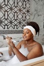 Side view on careful african woman doing manicure in bathtub at home