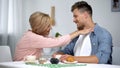 Careful mother putting napkin on son neck during having tea, overprotection Royalty Free Stock Photo