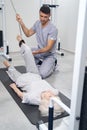 Careful orthopedic surgeon lifting pensioner leg with cable machine Royalty Free Stock Photo