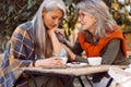 Careful senior woman calms dowm sad Asian friend spending time together in street cafe