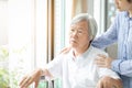 Caregiver asian daughter or young nurse standing behind the senior woman looking at window with hand on elder womanÃ¢â¬â¢s shoulder,