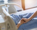 Caregiver and elderly senior patient (aged old adult person) holding hands in hospital bed or nursing hospice