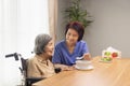 Caregiver feeding elderly asian woman with soup