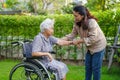 Caregiver help Asian elderly woman disability patient sitting on wheelchair in park, medical concept