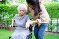 Caregiver help Asian elderly woman disability patient sitting on wheelchair in park, medical concept