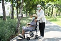 Caregiver help and care Asian senior or elderly old lady woman patient sitting on wheelchair and wear a face mask to travel in Royalty Free Stock Photo