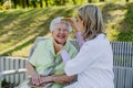 Caregiver helping senior woman to comb hair and make hairstyle when sitting on bench in park in summer. Royalty Free Stock Photo