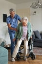 Caregiver helping senior woman to stand from her wheelchair in her home. Royalty Free Stock Photo