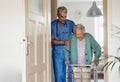 Caregiver helping senior woman to walk in her home with walker. Royalty Free Stock Photo