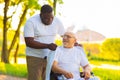 Caregiver and old man in a wheelchair. Professional nurse and patient walking outdoor in the park at sunset. Assistance Royalty Free Stock Photo