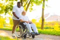 Caregiver and old man in a wheelchair. Professional nurse and patient walking outdoor in the park at sunset. Assistance Royalty Free Stock Photo