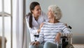 Caregiver supporting smiling disabled older woman sitting in wheelchair Royalty Free Stock Photo