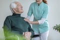 Caregiver talking to a happy man in a wheelchair in a nursing ho