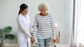 Caregiver teaching older woman to use walker at home