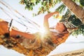 Careless blonde longhaired woman relaxing in hammock hinged between palm trees and playing with sun rays