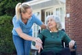 Carer Pushing Senior Woman In Wheelchair Outside Home